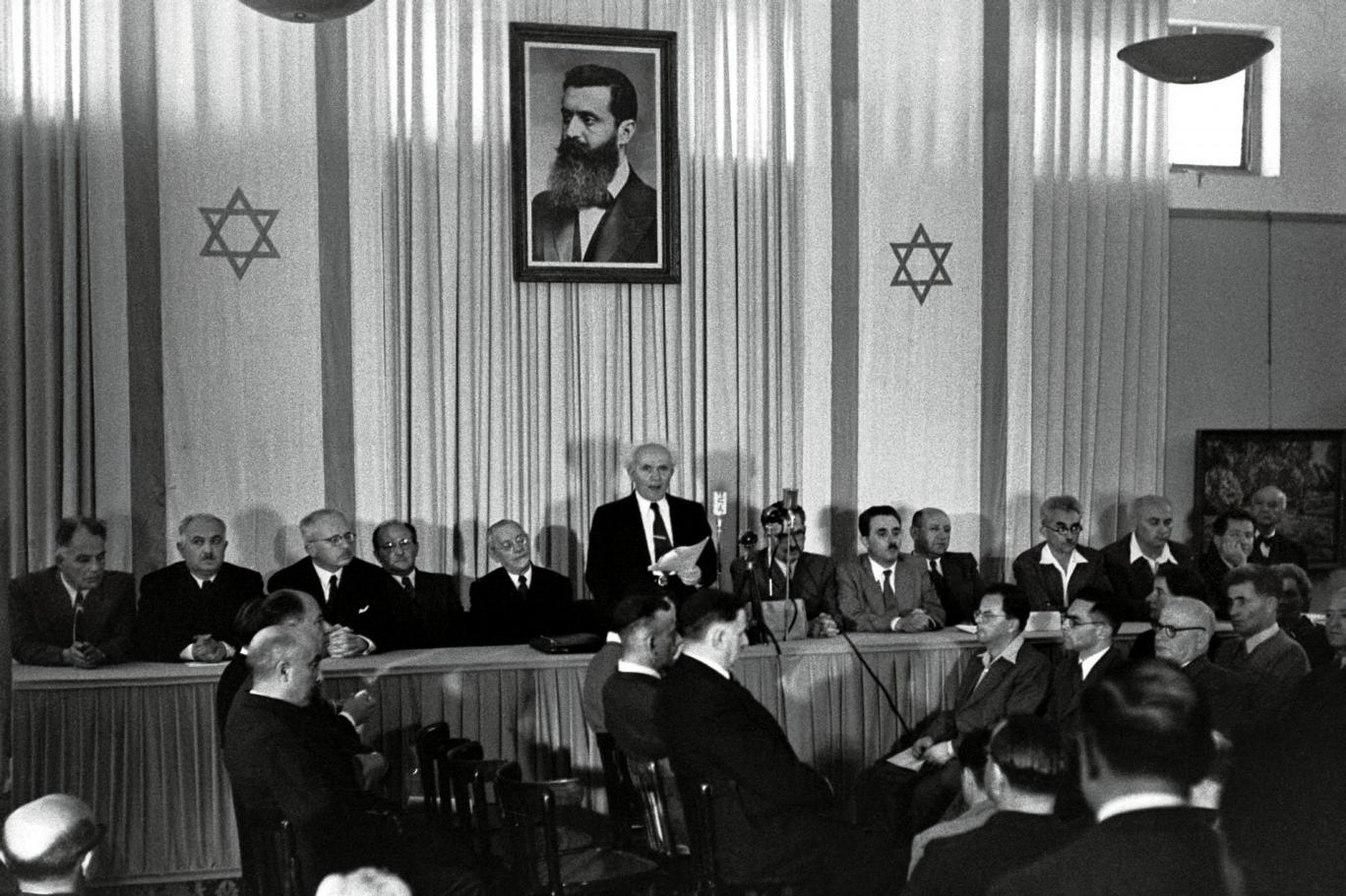 Nascila di una nazione. 1948: David Ben Gurion proclama la nascita di Israele con sopra la foto di Theodor Herzl